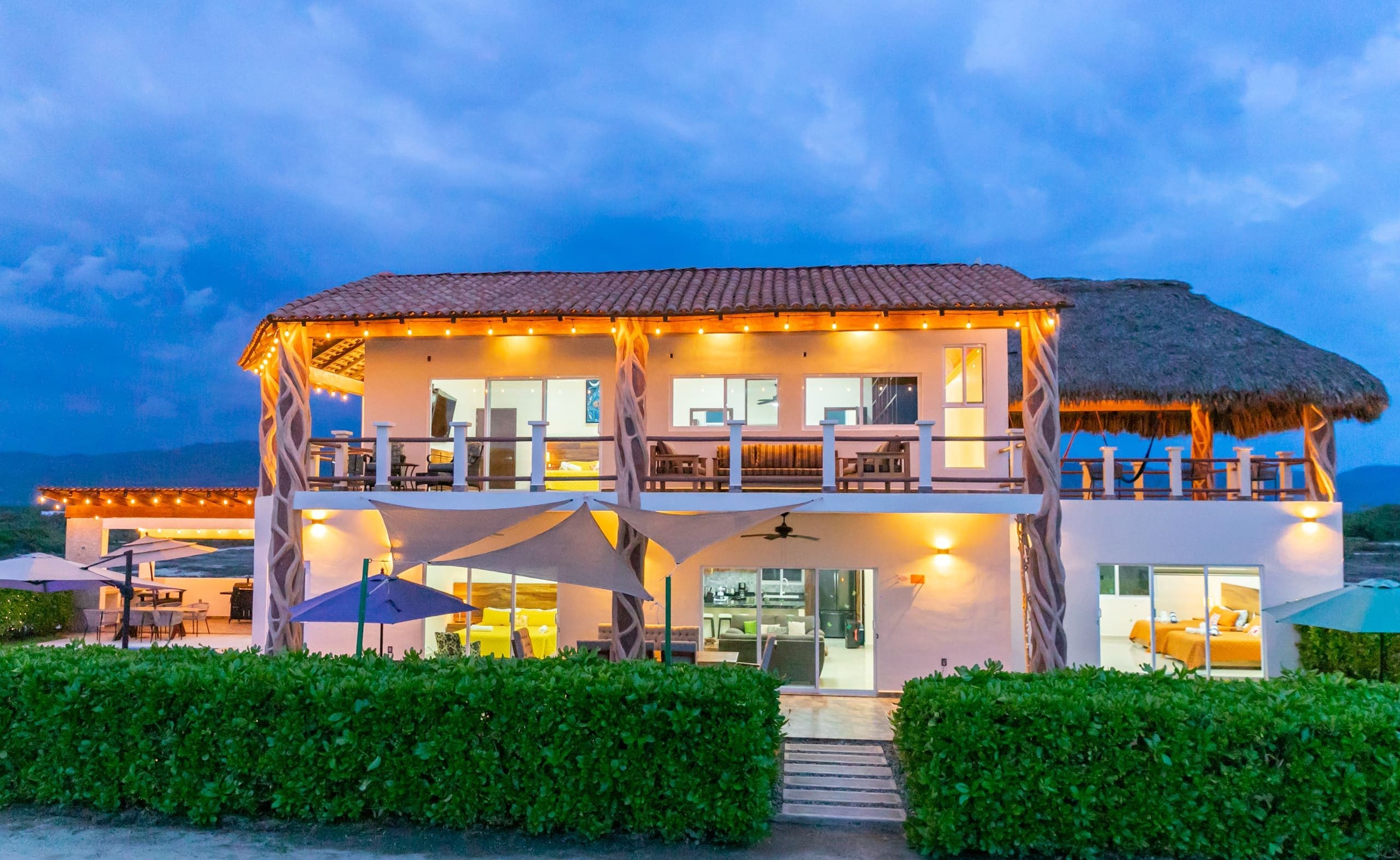 Casa Colores al atardecer frente al mar, con terrazas iluminadas y palapa
